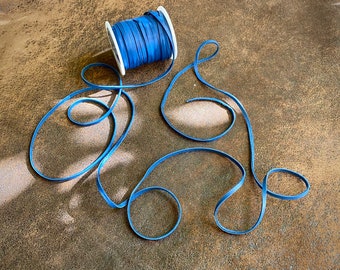 May include: A spool of blue ribbon with a white plastic center is on a brown surface. The ribbon is unraveled and forms a decorative design.