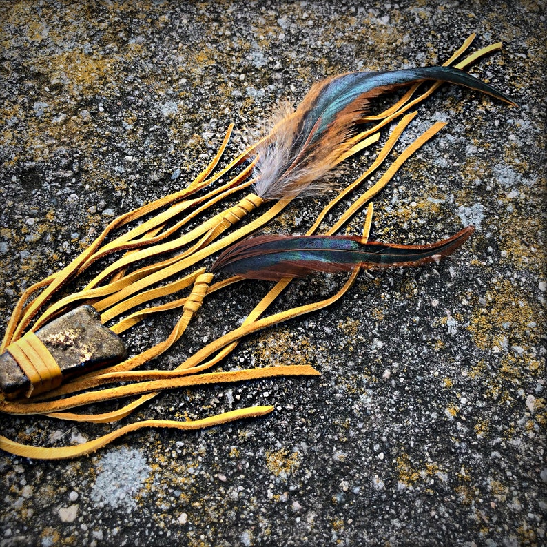 May include: A yellow leather fringe with a brown and blue feather attached to a brown leather wrapped stone.