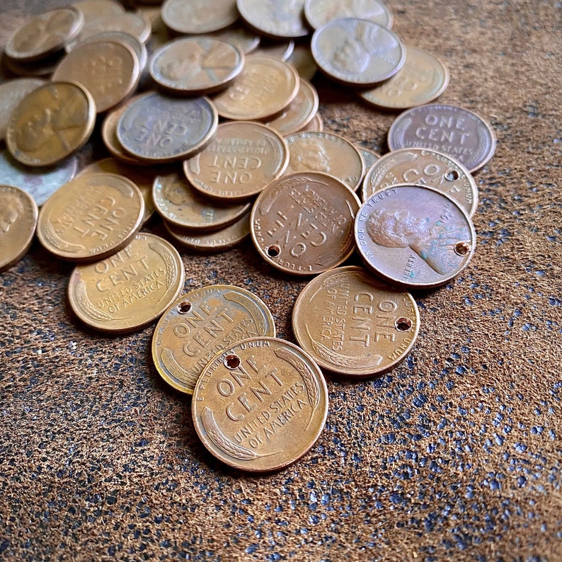 May include: A collection of copper-colored US one-cent coins, also known as pennies, with the words "One Cent" and "United States of America" inscribed on them. Some of the coins have a hole punched through the center.