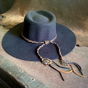 May include: A black felt wide-brimmed hat with a braided leather band and feather accents.