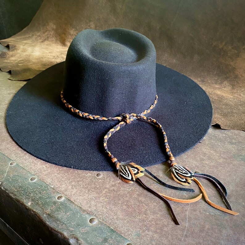 May include: A black felt wide-brimmed hat with a braided leather band and feather accents.