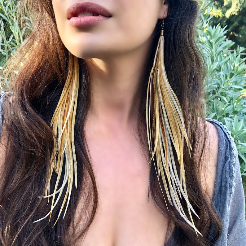 May include: Long, dangling feather earrings with a mix of brown, white, and gold feathers.