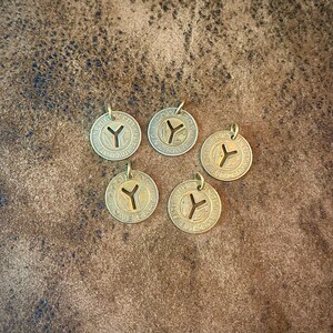 May include: Five vintage brass tokens with a circular design and a 'Y' symbol in the center. Each token has a small loop at the top for attaching to a chain or cord. The tokens are arranged on a textured brown surface.