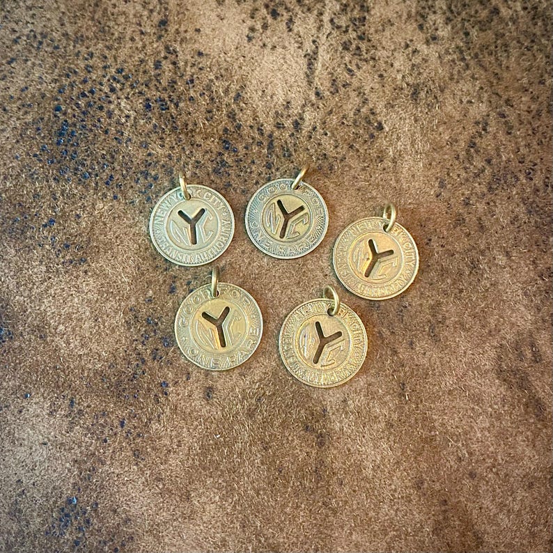 May include: Five vintage brass tokens with a circular design and a 'Y' symbol in the center. Each token has a small loop at the top for attaching to a chain or cord. The tokens are arranged on a textured brown surface.