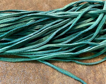 May include: Close-up of a bundle of teal-colored leather strips. The strips are thin, flexible, and have a slightly textured surface. The leather is a vibrant teal color, with variations in tone. The background is a brown, textured surface.