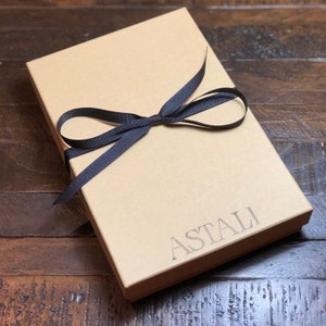 May include: A brown cardboard box with a black ribbon tied around it. The box is labeled "ASTALI".