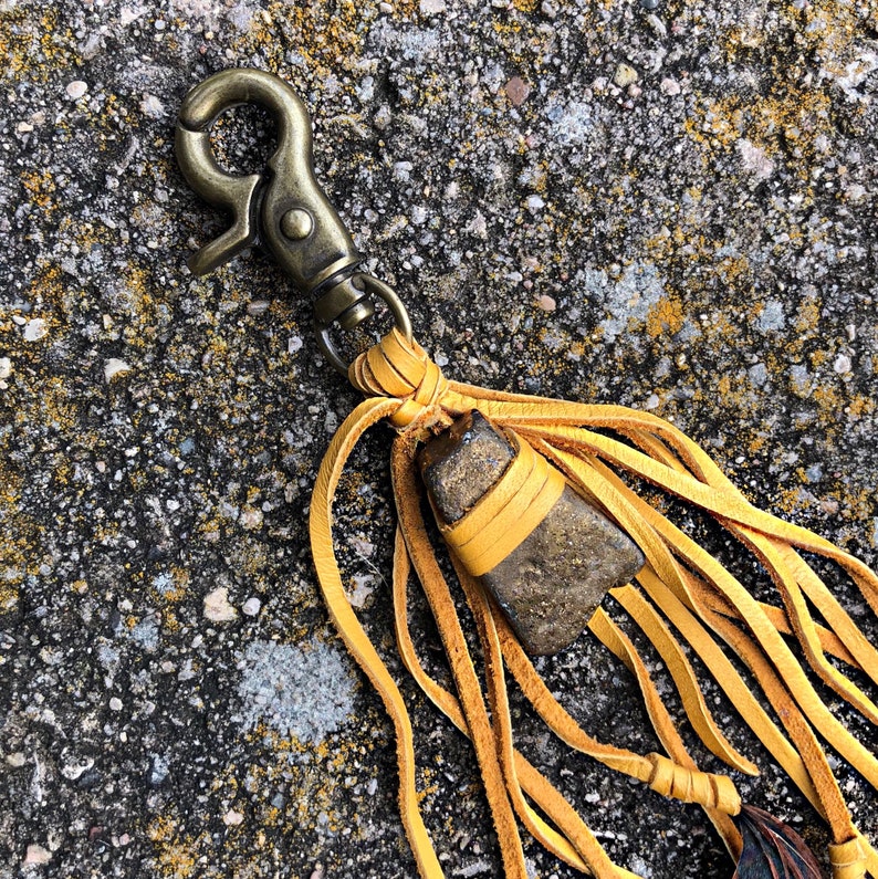 May include: A yellow leather tassel keychain with a brown stone and a brass clasp.