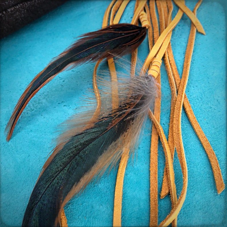 May include: Two long feathers with brown and green plumage, tied to a bundle of thin, yellow leather strips.