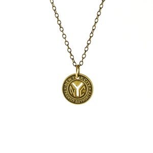 May include: A gold-colored necklace with a round pendant. The pendant features the text "NYC TRANSIT AUTHORITY" around the edge and the letters "NYC" in the center. The chain is a matching gold color.