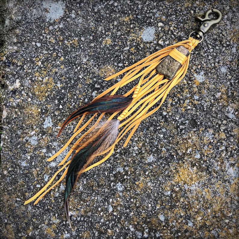 May include: A yellow leather keychain with a brown stone charm and two feathers. The keychain has a metal clasp.