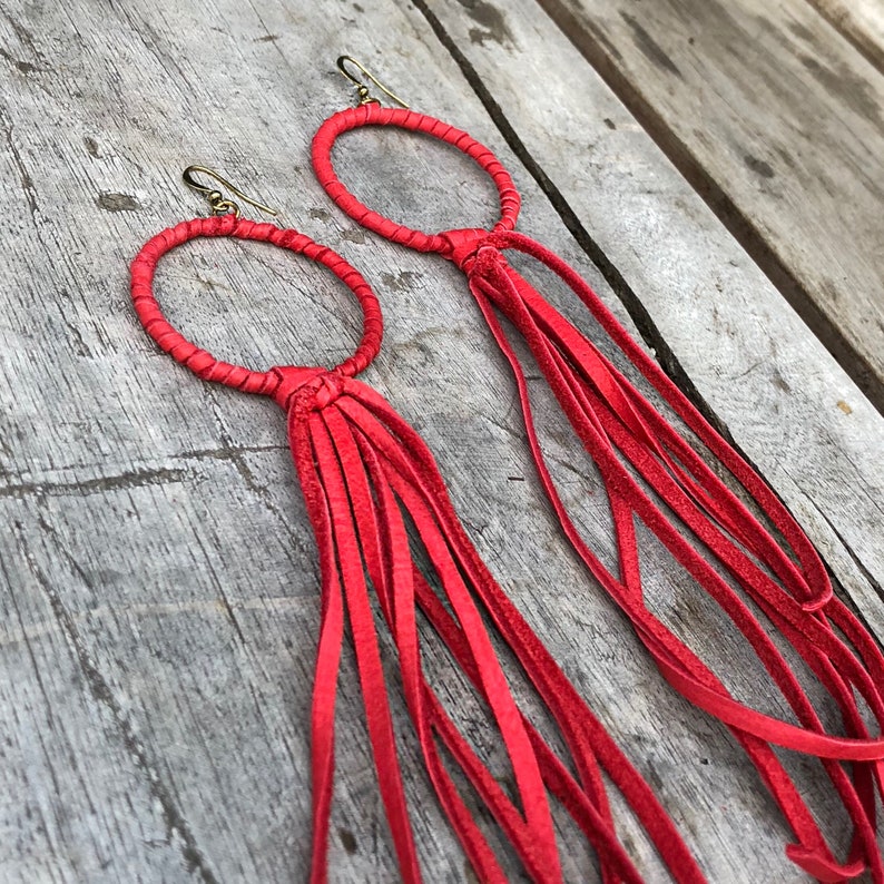 May include: A pair of red leather earrings with a circle design and long fringe tassels.