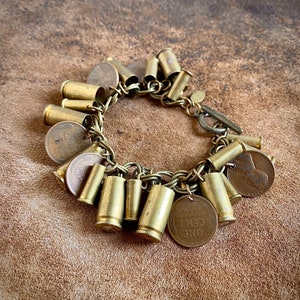 May include: A brass bracelet with multiple charms, including bullet casings and old US coins. The bracelet has a clasp closure.
