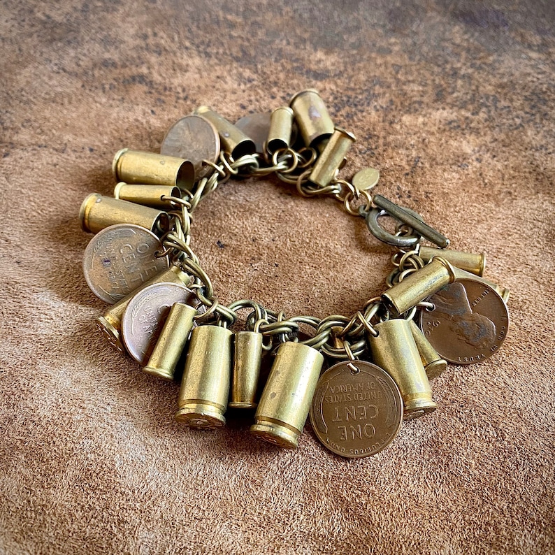 May include: A brass bracelet with multiple charms, including bullet casings and old US coins. The bracelet has a clasp closure.