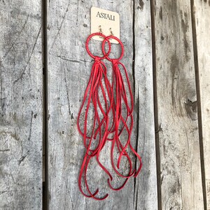 May include: Red leather earrings with a hoop design and long fringe tassels. The earrings are labelled "ASTALI" on a white tag.