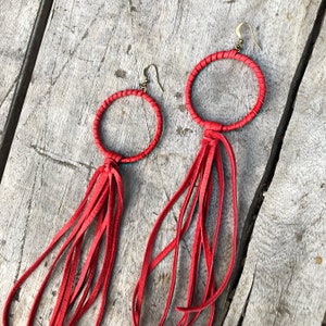 May include: A pair of red leather earrings with fringe tassels. The earrings are circular and have a simple design.