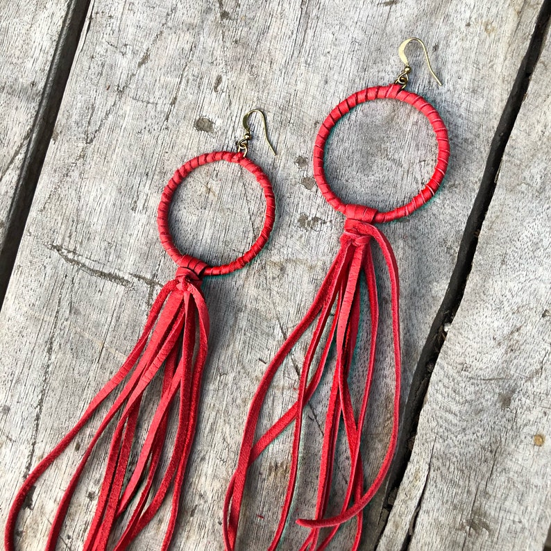 May include: A pair of red leather earrings with fringe tassels. The earrings are circular and have a simple design.