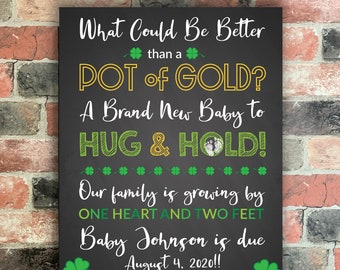 May include: Black chalkboard sign with green shamrocks and gold lettering announcing a new baby is due. The text reads "What Could Be Better than a POT of GOLD? A Brand New Baby to HUG & HOLD! Our family is growing by ONE HEART AND TWO FEET Baby Johnson is due August 4, 2020!! Allan, Melissa, Millie, & Jonah"