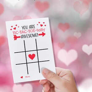 May include: A white Valentine's Day card with a red heart in the center of a tic-tac-toe board. The card reads "You are tic-tac-toe-tally awesome!" with a red arrow pointing to the right. The card also has the words "From:" at the bottom.
