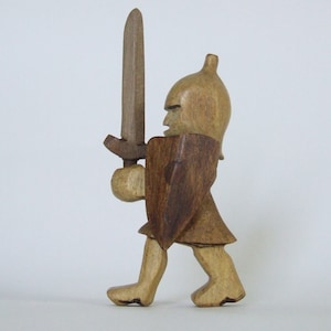 May include: A wooden figurine of a knight in armour, holding a sword and walking forward. The knight is carved from light and dark brown wood.