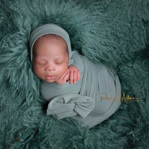 May include: A newborn baby is swaddled in a light green fabric and sleeping on a soft, green fuzzy blanket.