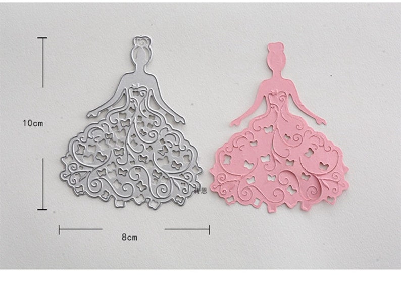 Puede incluir: Dos plantillas de metal troqueladas de una princesa con un vestido con intrincados dise&ntilde;os florales. Las plantillas miden 10 cm de alto y 8 cm de ancho.