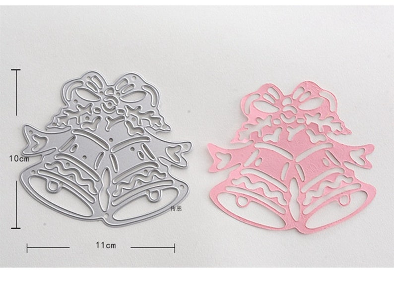 Puede incluir: Una matriz de corte de metal para proyectos de manualidades que presenta dos campanas con lazos y un dise&ntilde;o decorativo. La matriz mide 10 cm por 11 cm.