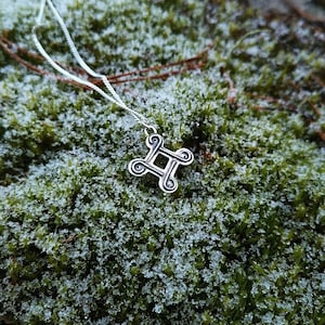 May include: A silver necklace with a Celtic knot pendant, resting on a bed of green moss covered in frost.