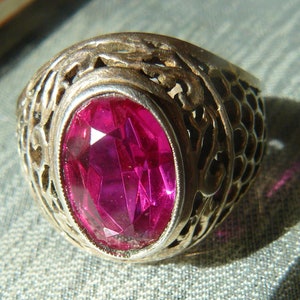 Op de afbeelding: Een zilveren ring met een sierlijk ontwerp en een grote, gefacetteerde, roze edelsteen.