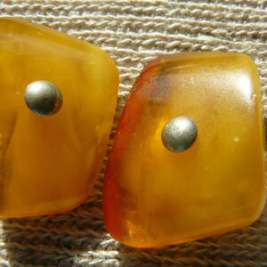 May include: Two amber-colored, teardrop-shaped earrings with silver accents. The earrings have a smooth, polished finish.