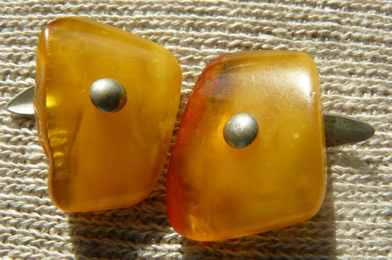 May include: Two amber-colored, teardrop-shaped earrings with silver accents. The earrings have a smooth, polished finish.