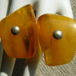 May include: A pair of amber-colored earrings with silver accents. The earrings are teardrop shaped and have a smooth, polished finish.