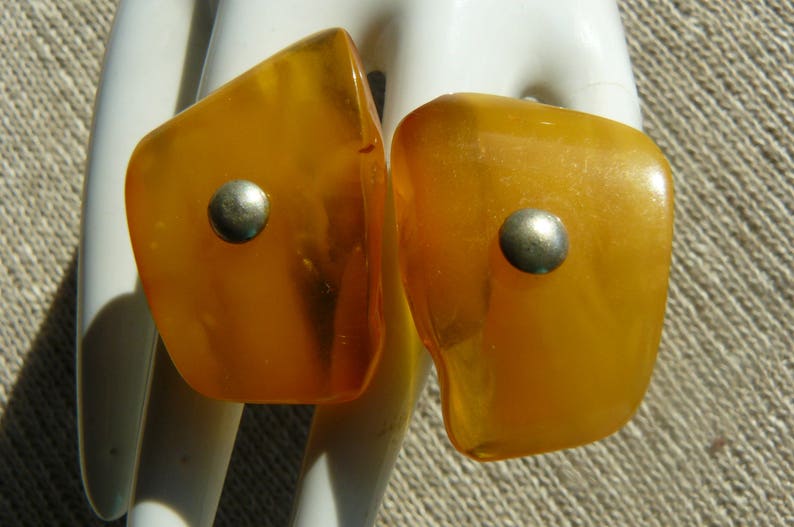 May include: A pair of amber-colored earrings with silver accents. The earrings are teardrop shaped and have a smooth, polished finish.