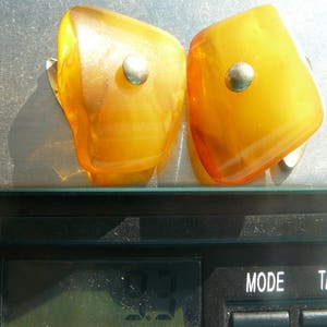 May include: Two amber-colored earrings with silver accents. The earrings are shaped like a teardrop and have a smooth, polished finish.