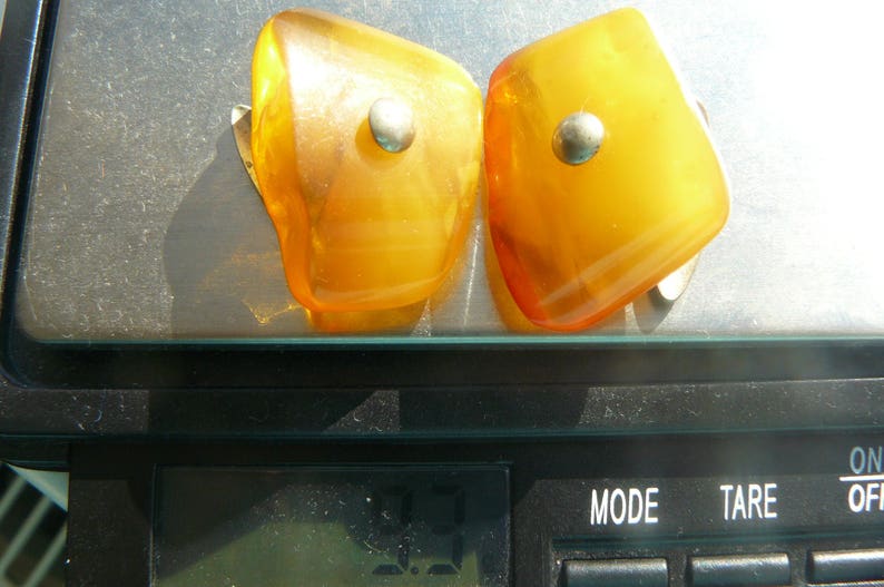 May include: Two amber-colored earrings with silver accents. The earrings are shaped like a teardrop and have a smooth, polished finish.