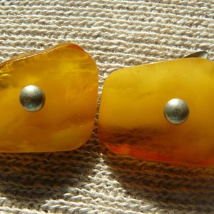 May include: Two amber-colored earrings with silver accents. Each earring has a round, silver-colored metal piece in the center.