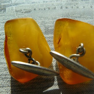 May include: A pair of amber cufflinks with silver accents. The cufflinks are irregularly shaped and have a polished finish.