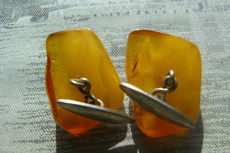 May include: A pair of amber cufflinks with silver accents. The cufflinks are irregularly shaped and have a polished finish.