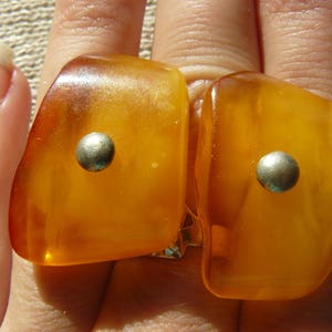 May include: Two amber-colored rings with silver accents. The rings are worn on the fingers of a hand.