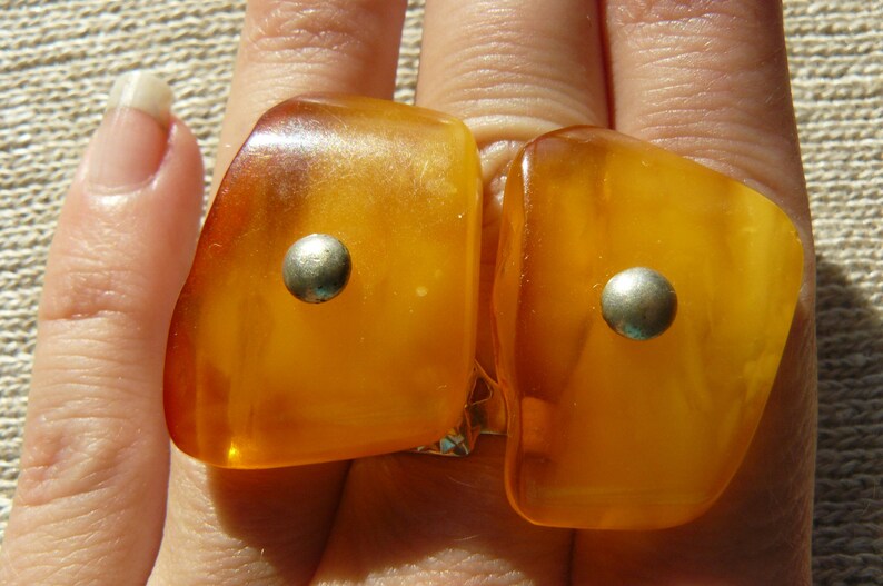 May include: Two amber-colored rings with silver accents. The rings are worn on the fingers of a hand.
