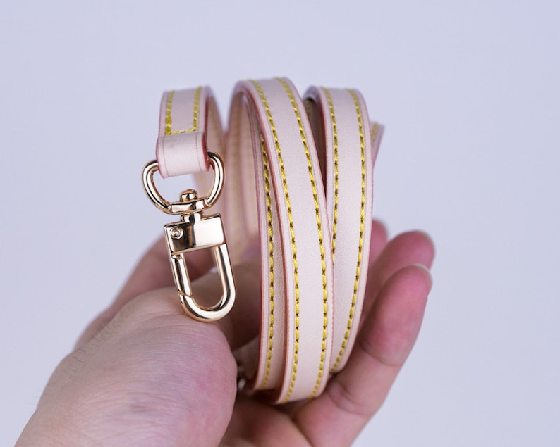 May include: A light pink leather strap with gold stitching and a gold metal clasp.