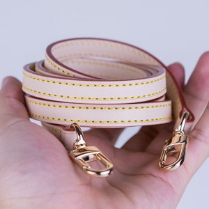 May include: A beige leather strap with gold-tone hardware. The strap is folded in half and has a double row of stitching.