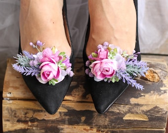 May include: A pair of black pointed-toe shoes with floral embellishments. The flowers are pink, purple, and white, and they are arranged in a cluster on the top of each shoe.