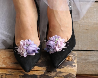 May include: A pair of black suede shoes with delicate purple and pink flower embellishments on the toes.