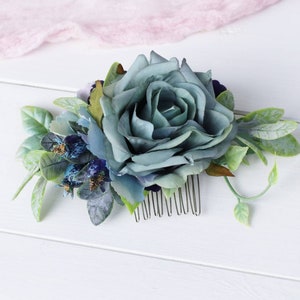 Op de afbeelding: Een blauwe en groene bloemenhaar kam met een grote blauwe roos en kleinere blauwe bloemen. De kam is gemaakt van metaal en heeft een zilveren afwerking.