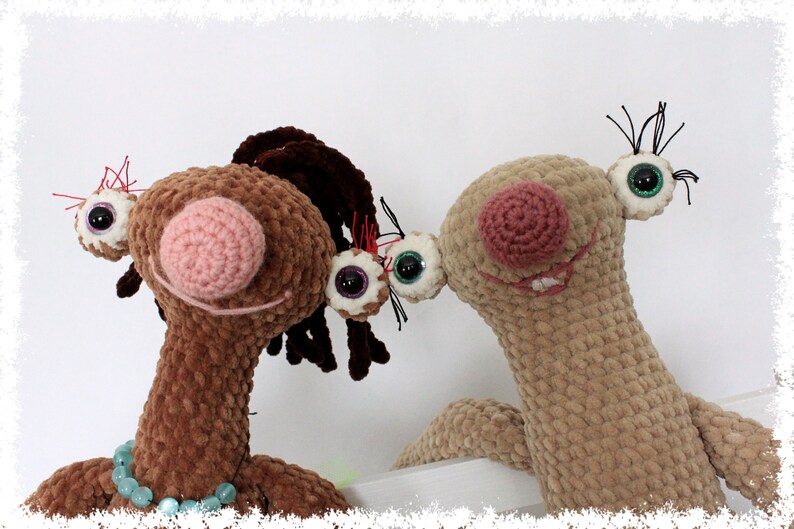 May include: Two crocheted plush toys with large eyes and pink noses. The brown toy has brown hair and is wearing a turquoise beaded necklace. The beige toy has black eyelashes.