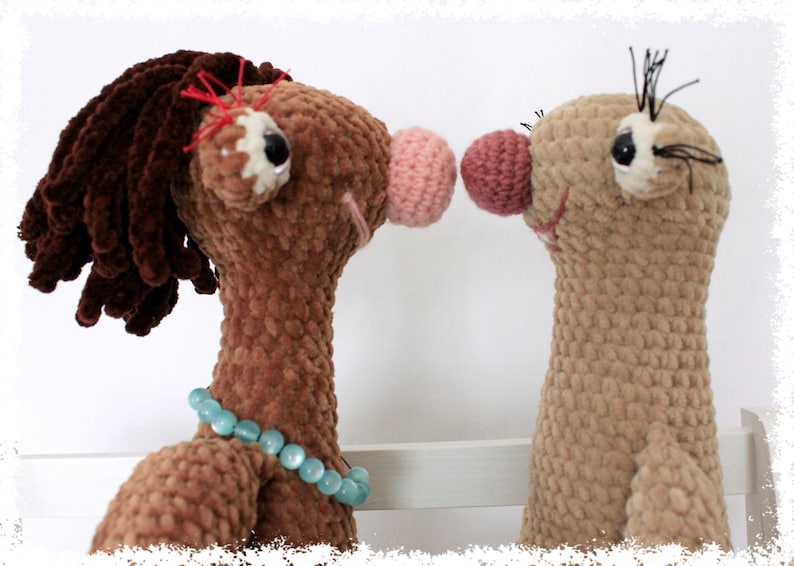 May include: Two crocheted stuffed animals, one brown with a blue beaded necklace and a pink nose, the other tan with a pink nose, facing each other.
