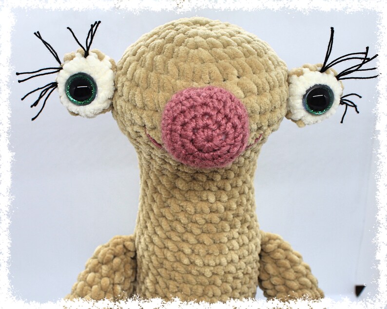 May include: A crocheted plush toy with a brown body, pink nose, and large green eyes. The toy has black yarn for eyelashes.