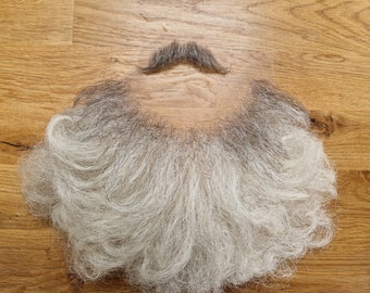 May include: A white and gray fake beard with a mustache on a wooden surface.