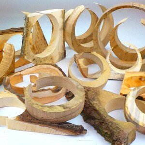 Könnte beinhalten: Eine Sammlung von Holzringen und anderen Formen, die alle aus dem gleichen Holz geschnitzt sind. Das Holz hat eine natürliche, hellbraune Farbe und eine glatte, polierte Oberfläche. Die Ringe sind in verschiedenen Größen und Formen vorhanden, und einige wurden mit komplizierten Designs geschnitzt.