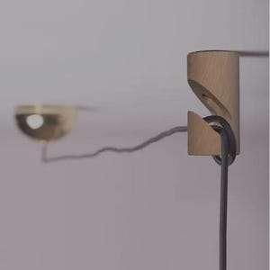 Könnte beinhalten: Eine moderne Leuchte mit Holzhalterung und einer messingfarbenen Glühbirne. Die Leuchte hat ein dunkelgraues Kabel, das durch die Holzhalterung geschlungen ist. Das Design ist minimalistisch und modern, passend für verschiedene Einrichtungsstile.